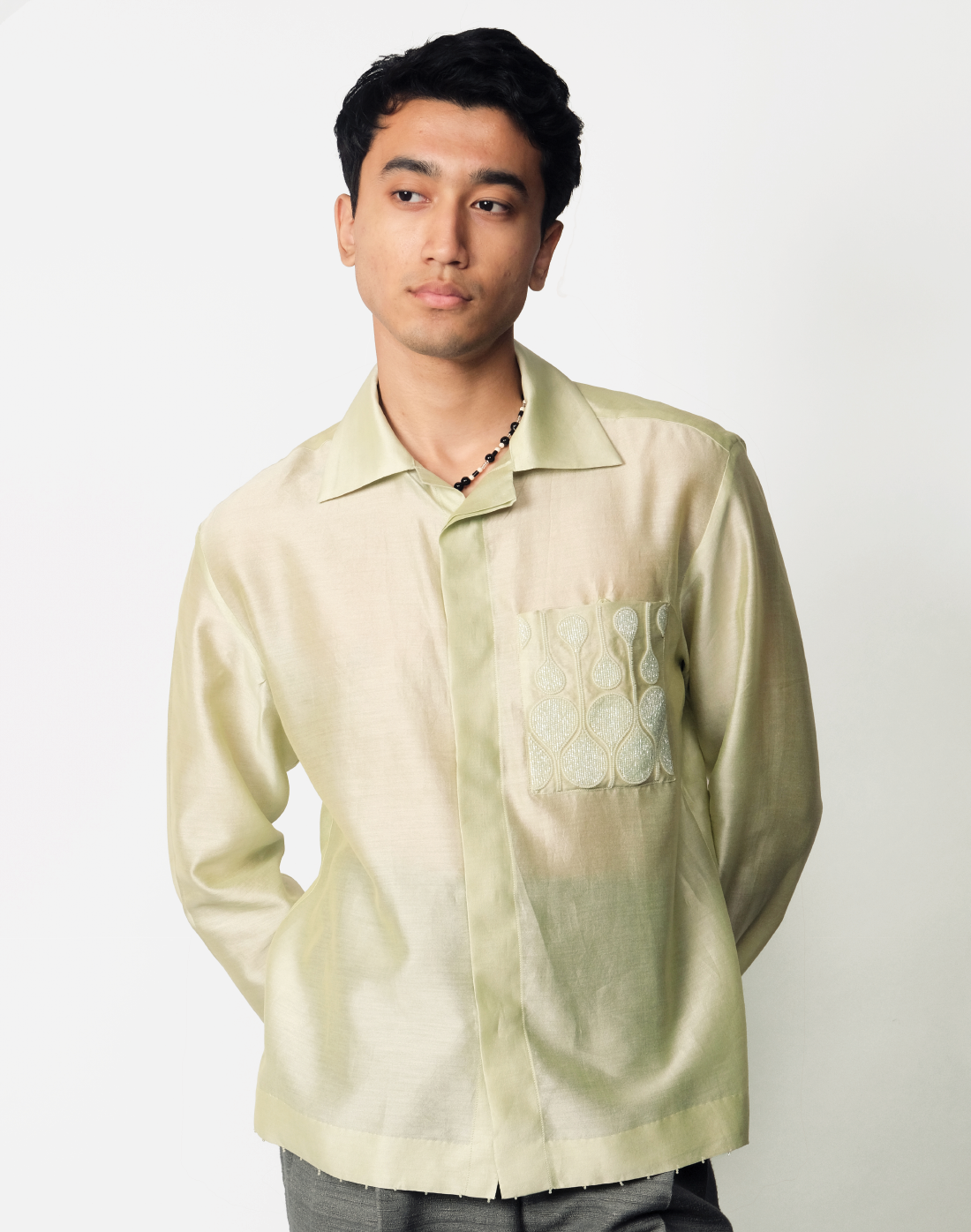 Pale green relaxed Chanderi silk shirt featuring hand embroidered logo-inspired pocket and glass bead trim by Taarini Anand front