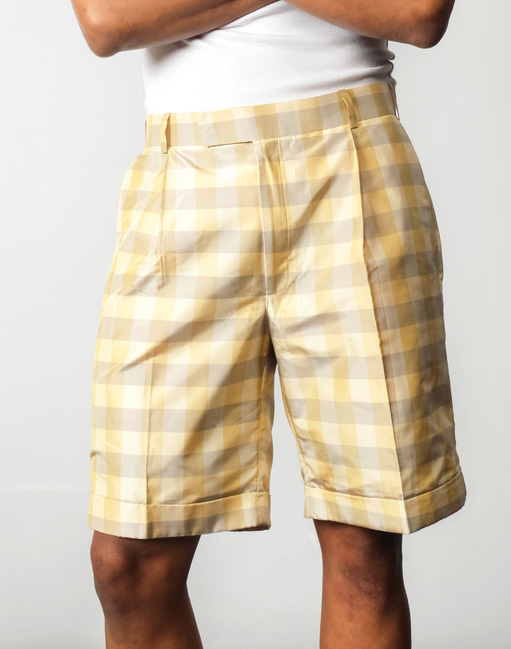 Front view of handwoven silk gingham taffeta pleated shorts, in a green and yellow check pattern.