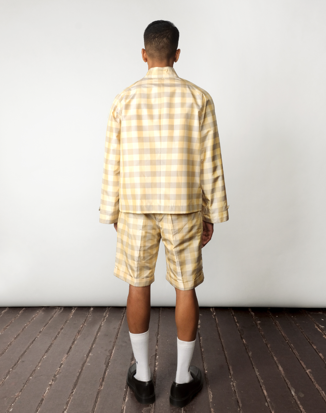 Back view of handwoven silk gingham taffeta raglan jacket with pleated shorts, in a green and yellow check pattern.
