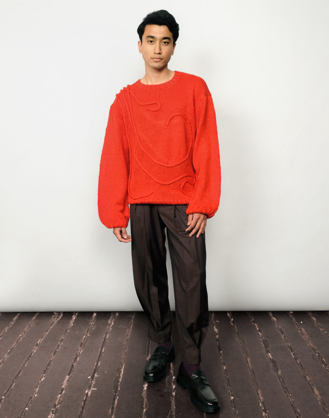 Bright red hand-knit Inferno Sweater styled with black Double Box Pleat Trousers by Taarini Anand
